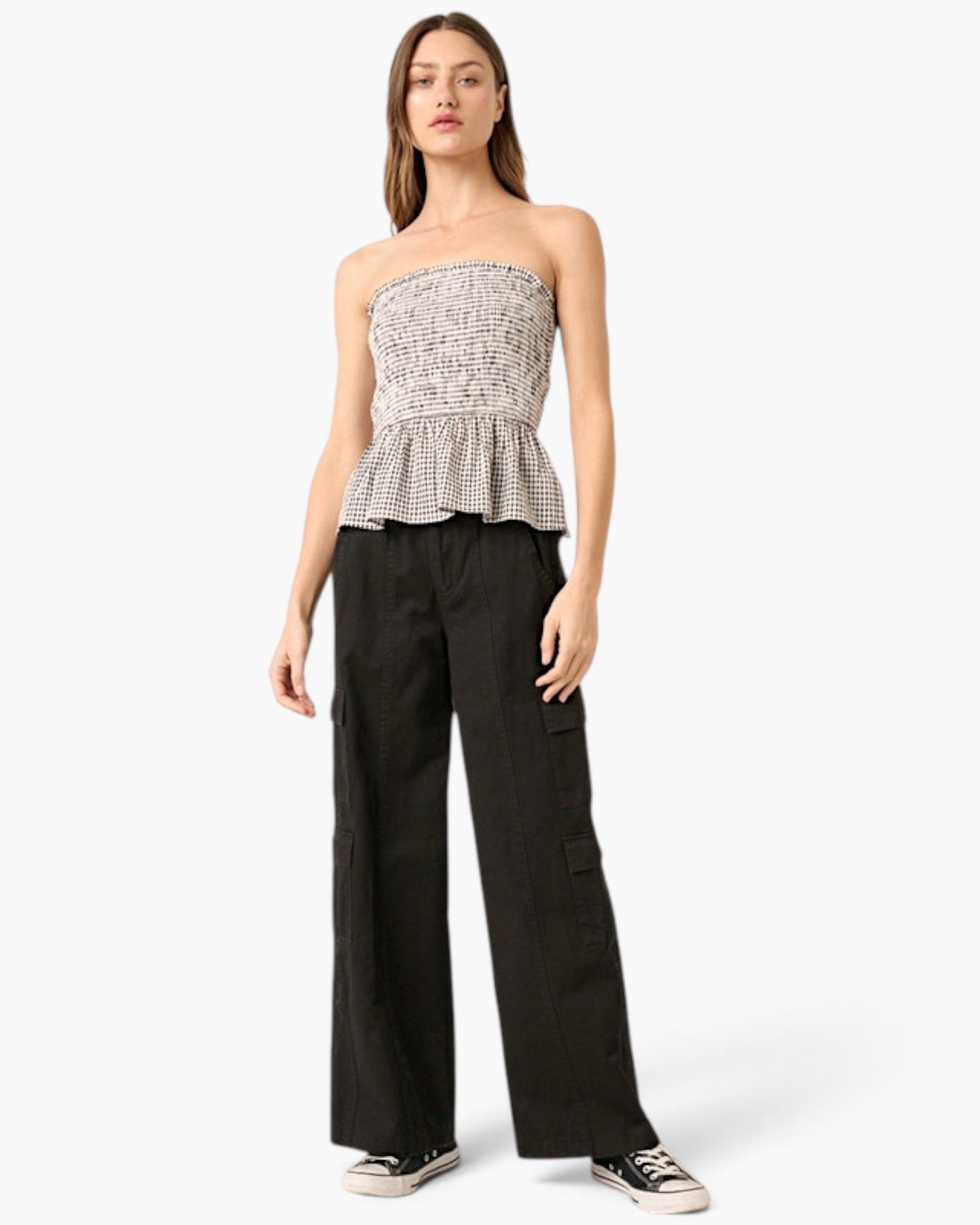 A woman modeling a strapless black and white patterned peplum top paired with black wide-leg cargo pants and black sneakers, set against a plain white studio background.