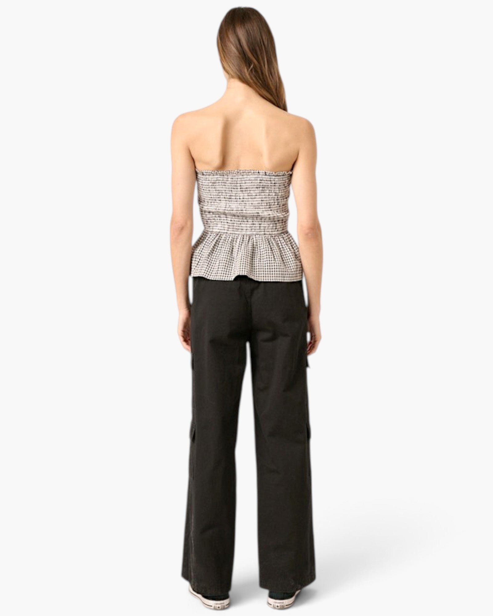 A woman shown from the back wearing a strapless black and white patterned peplum top and black wide-leg pants, photographed against a light gray studio background.