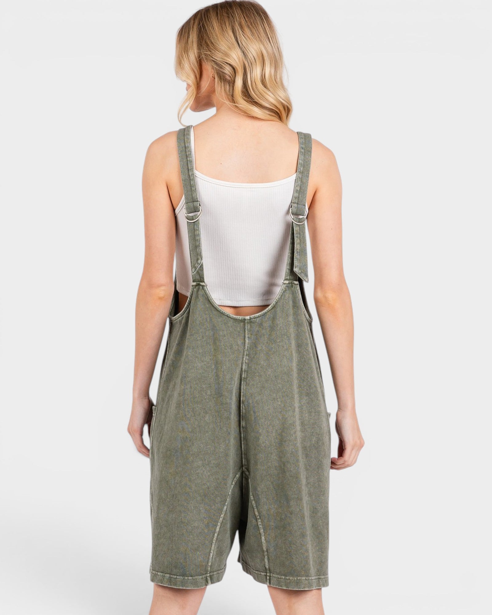 Person wearing a green denim overall dress on a white background