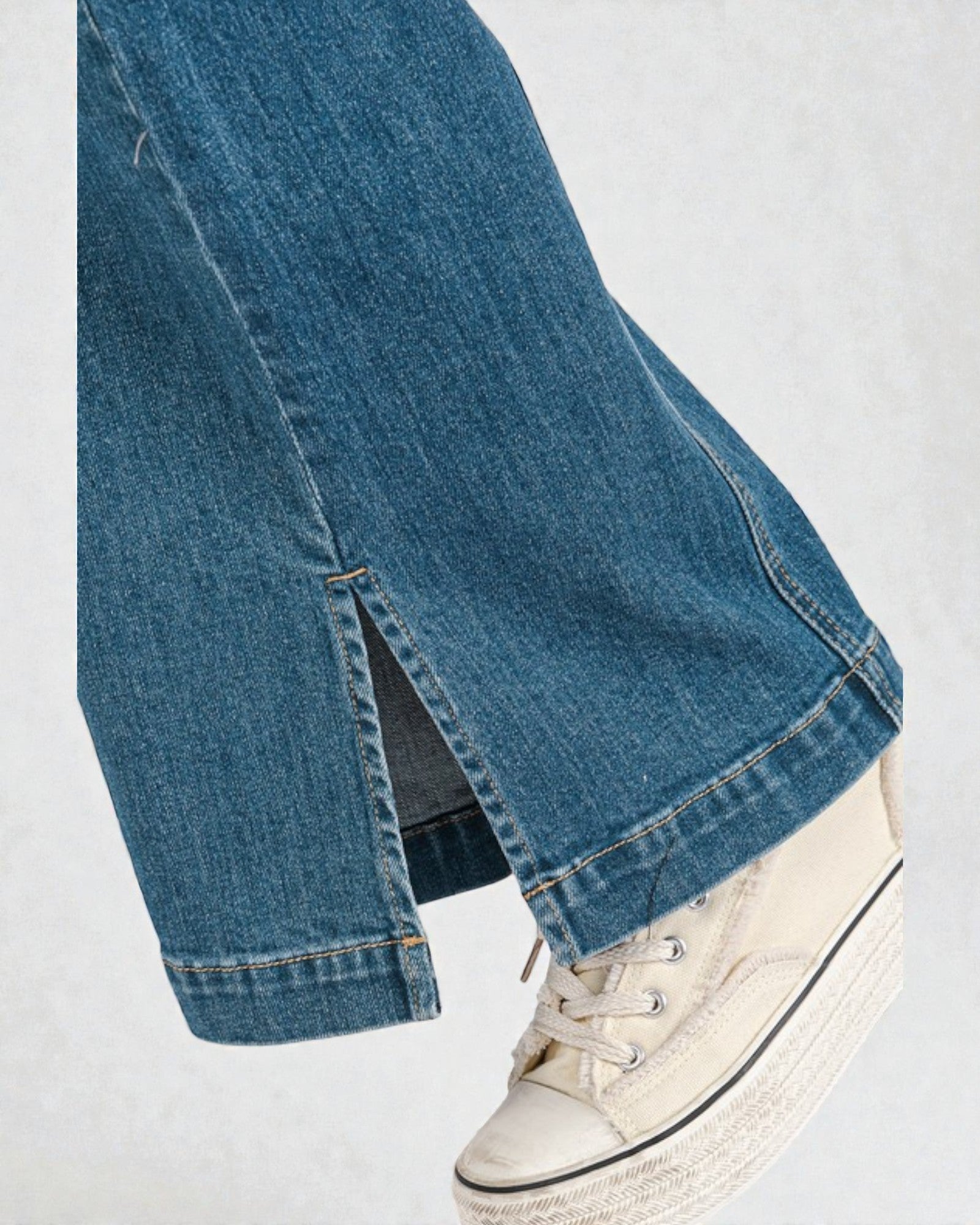 Close-up of blue jeans with a white sneaker on a light gray background