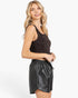 A woman modeling a dark brown sleeveless crop top and black faux-leather mini skirt against a plain white studio background.