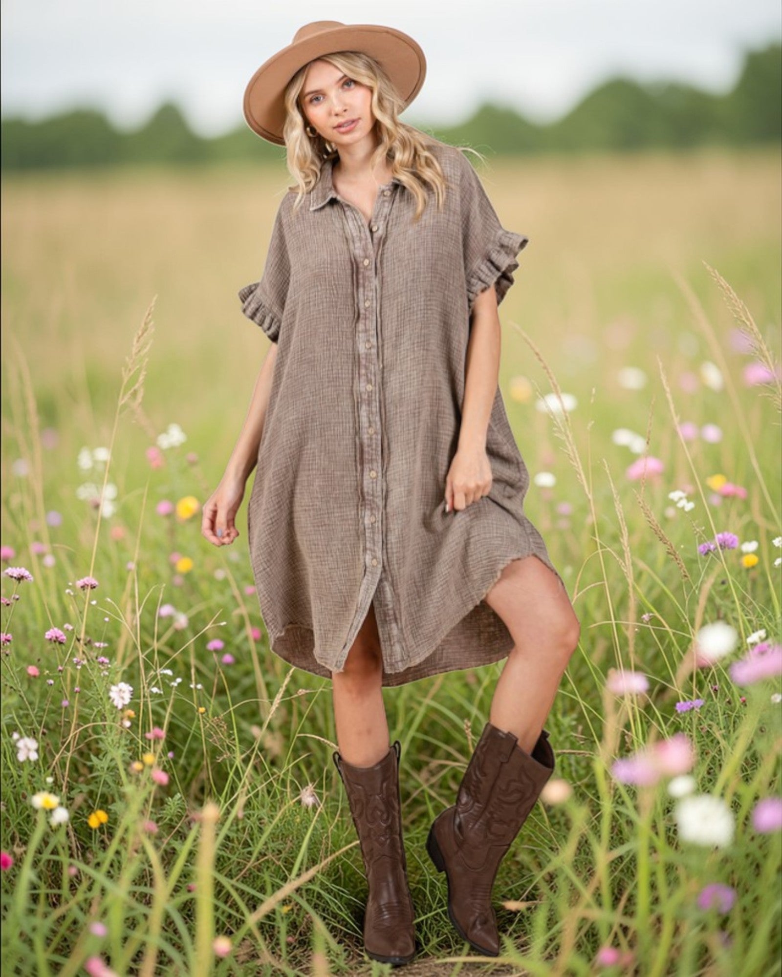Woman in a brown dress and hat standing in a field of wildflowers