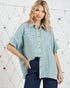 Woman wearing a light blue checkered shirt with a white geometric patterned wall in the background