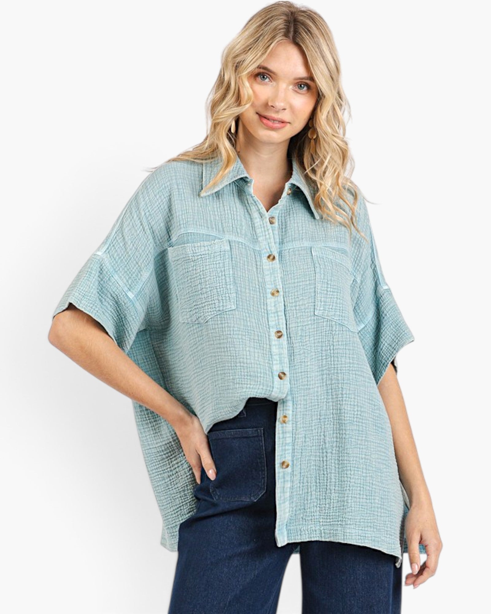 A woman wearing a light blue-green textured short-sleeve button-up shirt with two chest pockets and dark blue jeans, photographed against a clean white studio background.