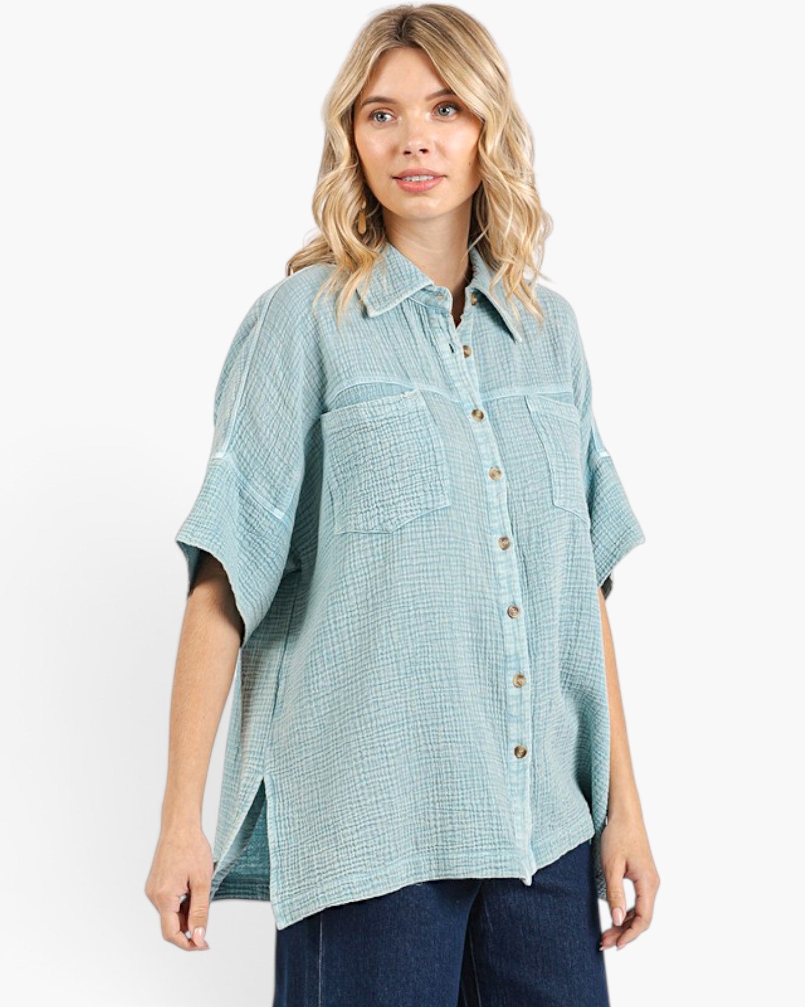 A woman wearing a light blue-green textured short-sleeve button-up shirt with dark blue jeans, photographed against a clean white studio background.