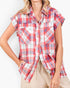 A woman wearing a red, white, and blue plaid short-sleeve button-up shirt with chest pockets, paired with beige drawstring pants, against a plain white background.