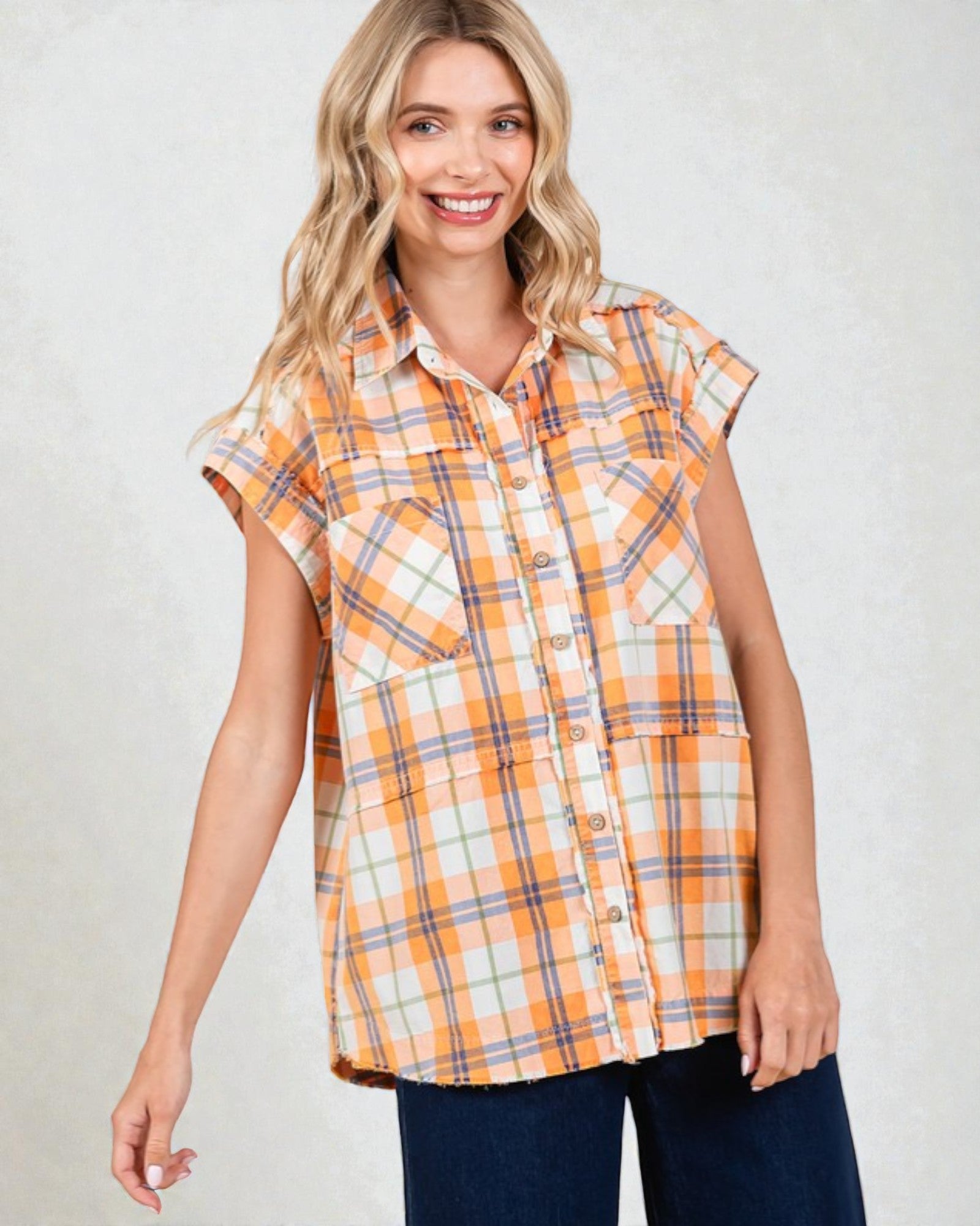 Woman wearing an orange and blue plaid sleeveless shirt against a plain background