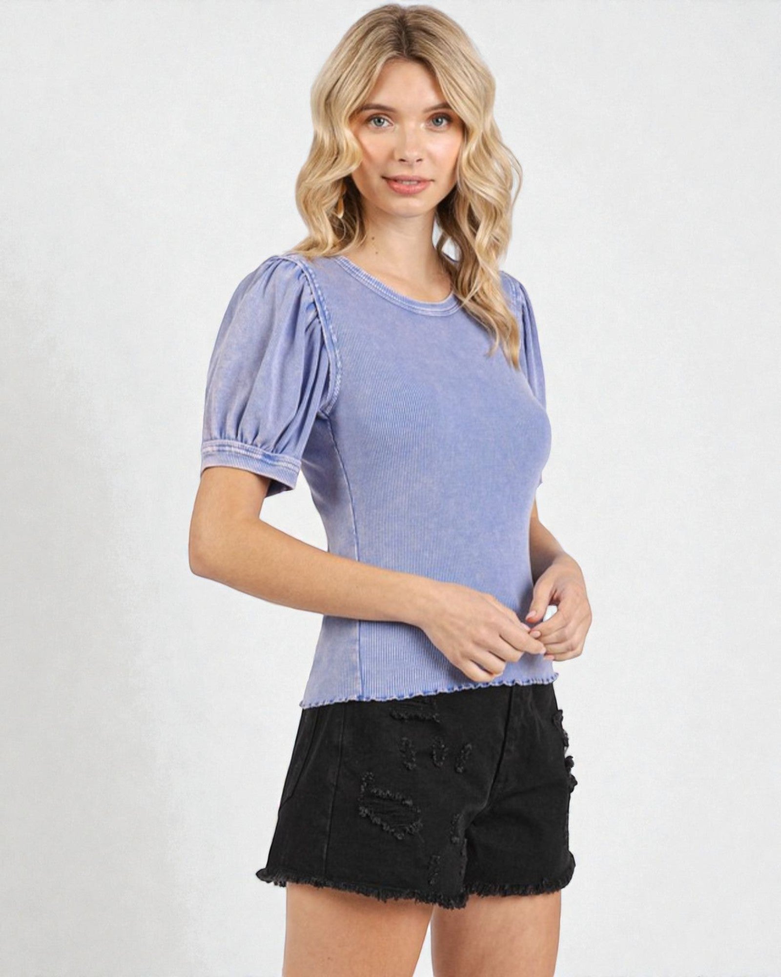 Woman wearing a blue top with puffed sleeves and black shorts on a white background