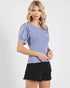 Woman wearing a blue top with puffed sleeves and black shorts on a white background