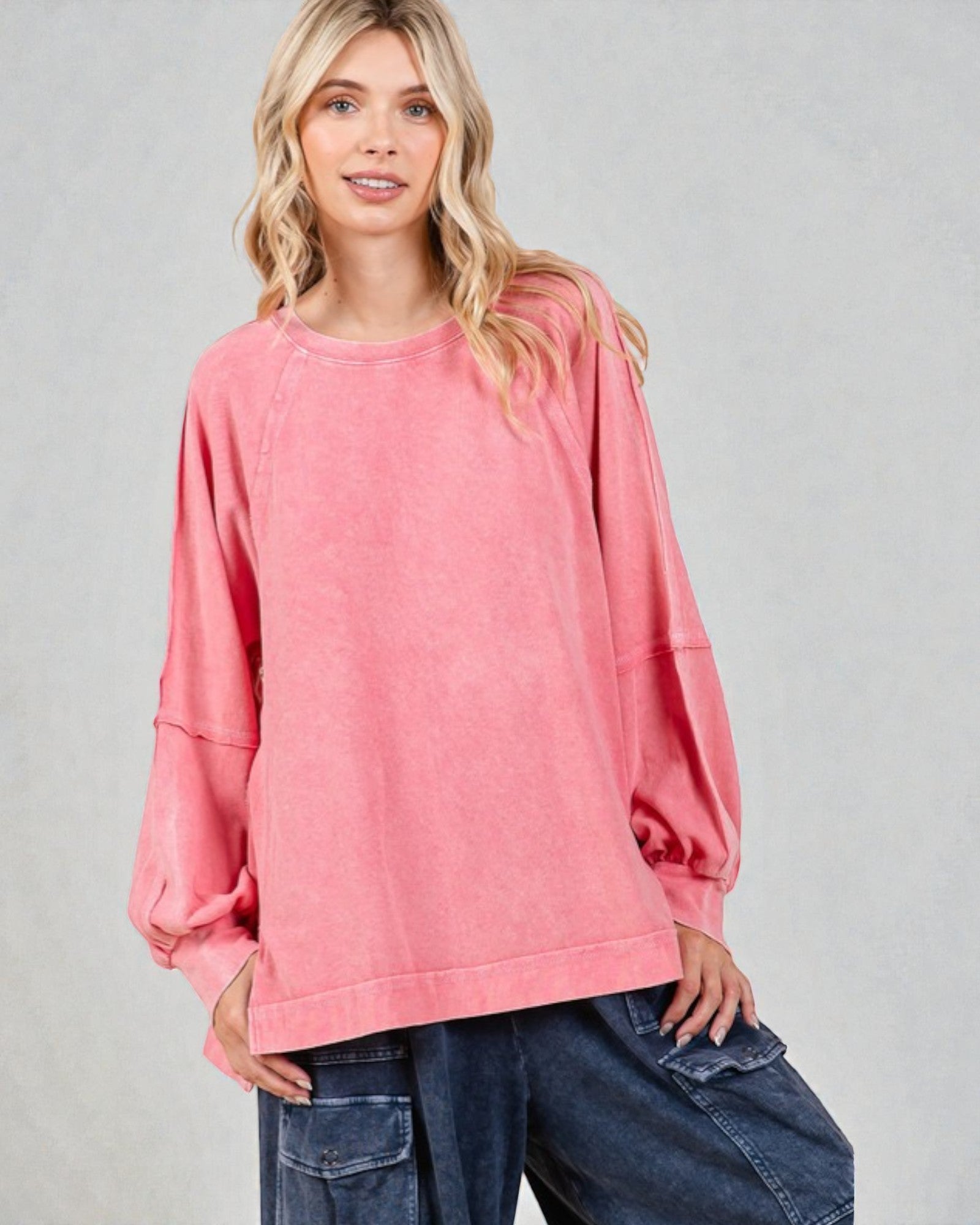 Woman wearing a pink oversized sweater and blue jeans on a gray background