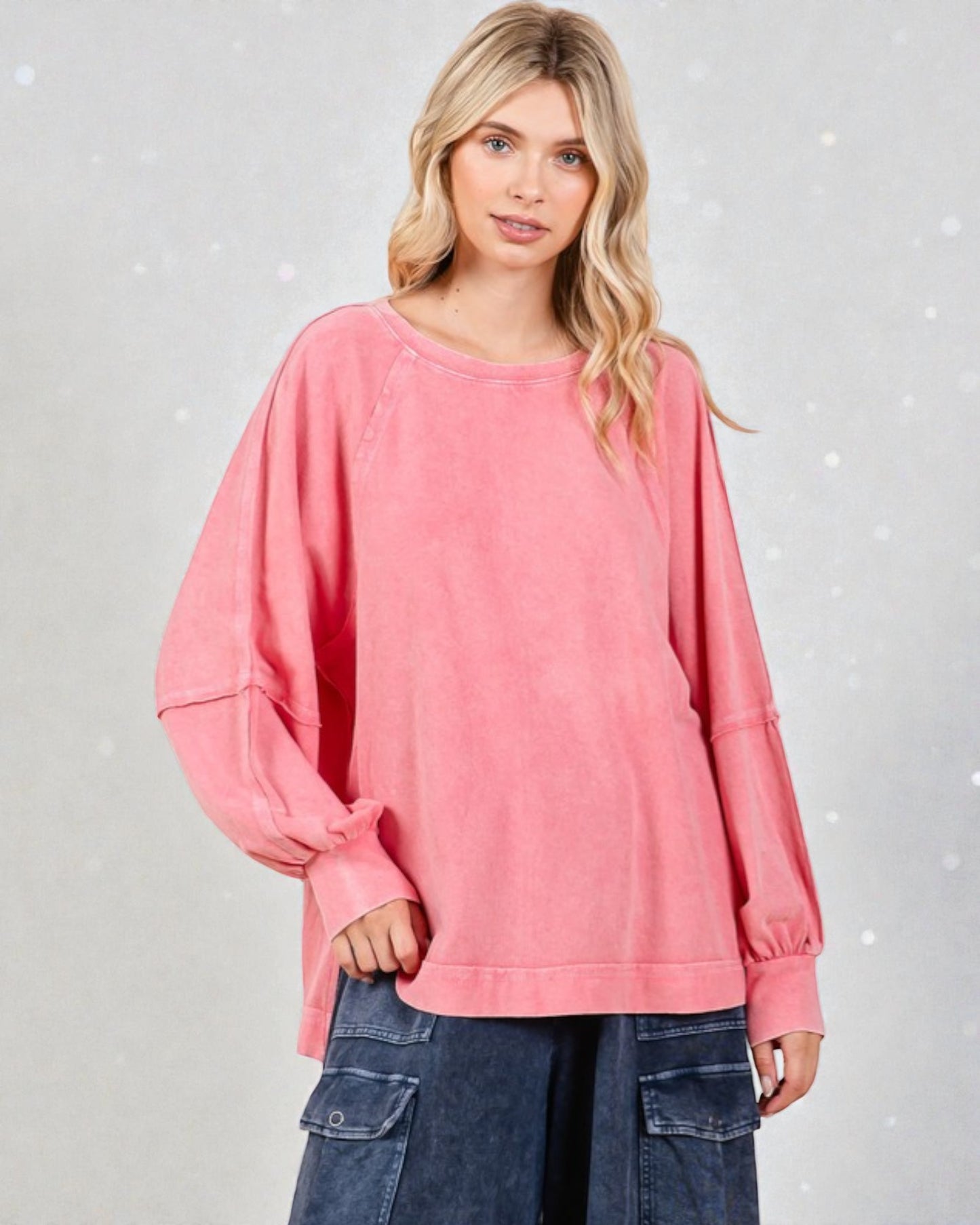 Woman wearing a pink oversized sweater with blue jeans on a light gray background