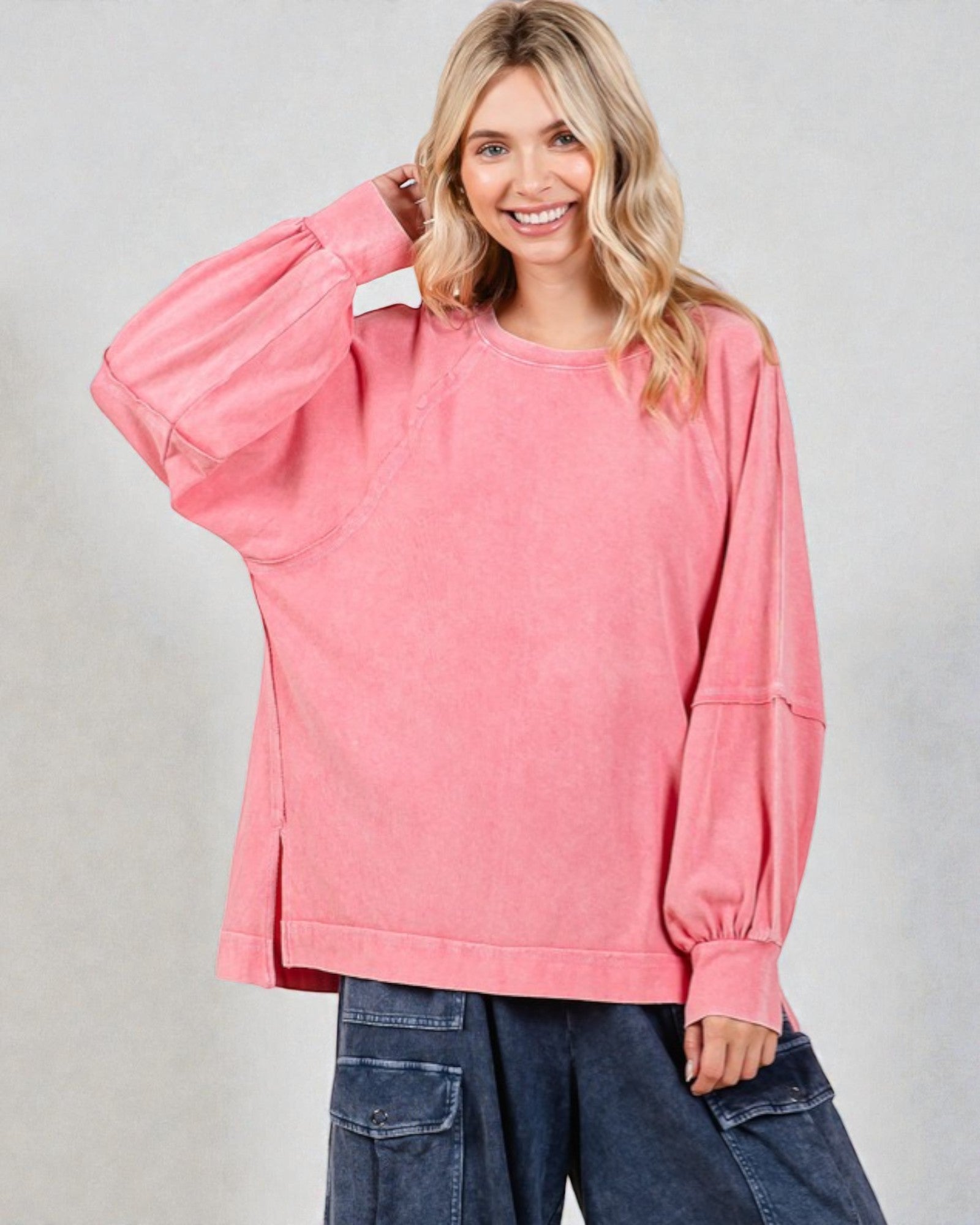 Woman wearing a pink oversized sweatshirt and blue jeans against a gray background