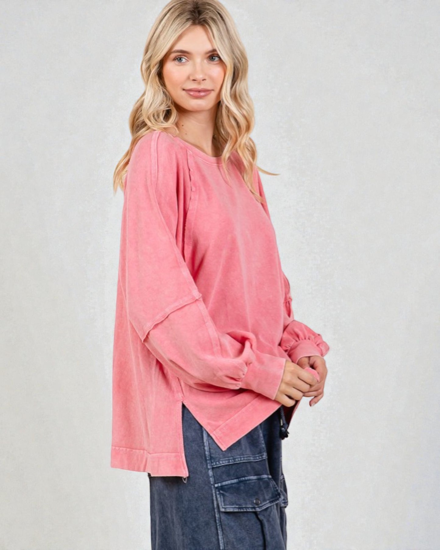 Woman wearing a pink oversized top and blue jeans on a plain background