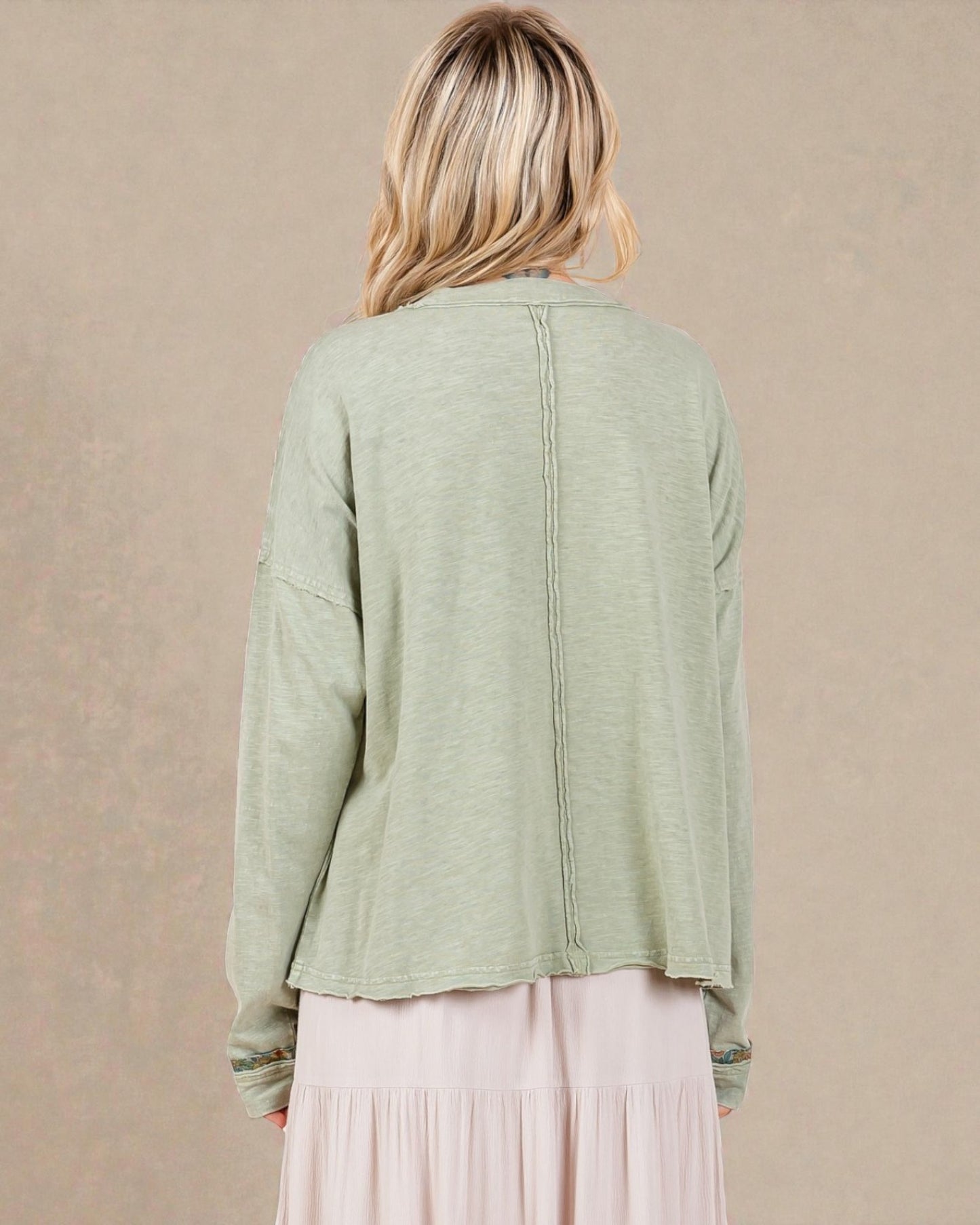 Person wearing a light green cardigan over a pink dress on a beige background