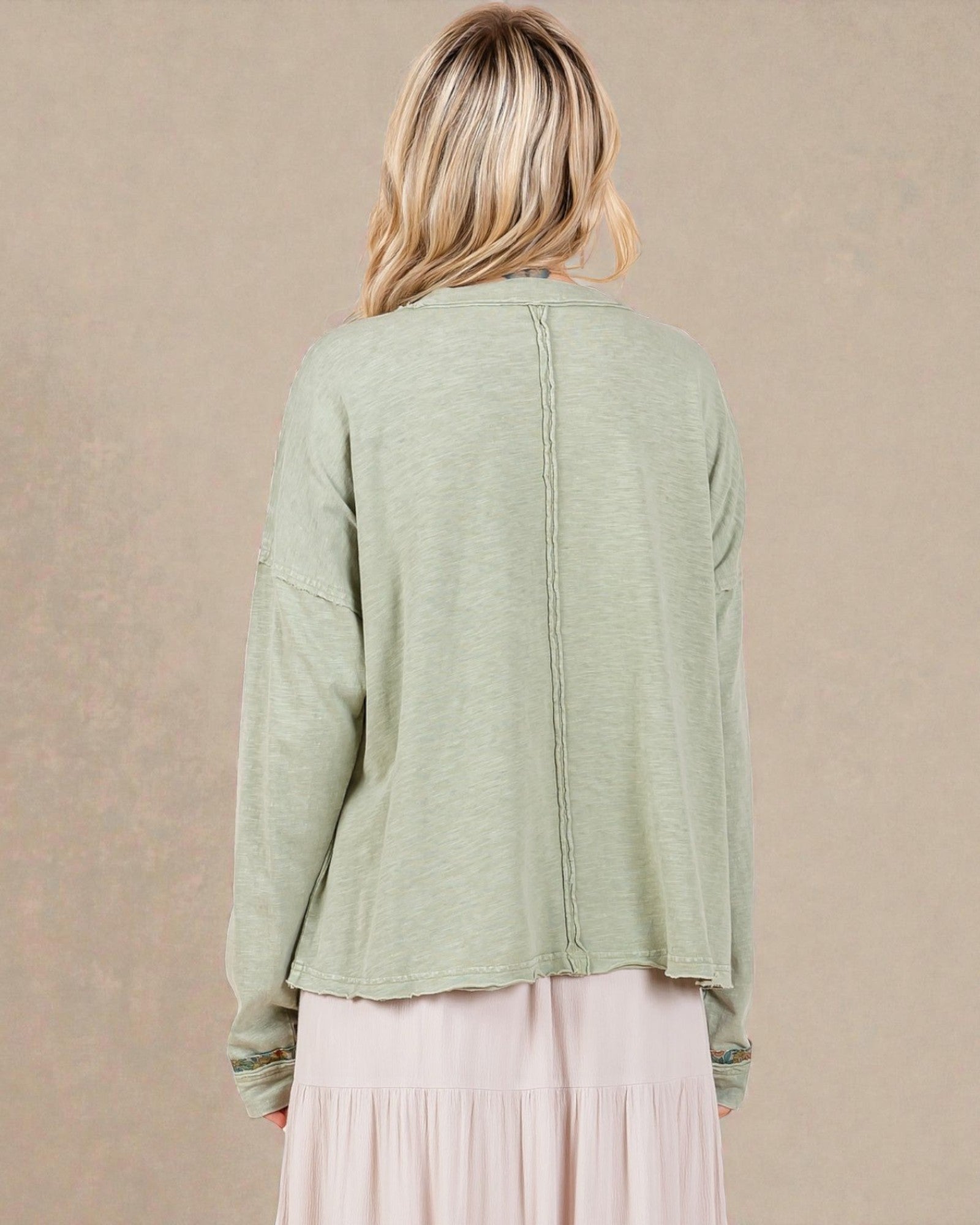 Person wearing a light green cardigan over a pink dress on a beige background