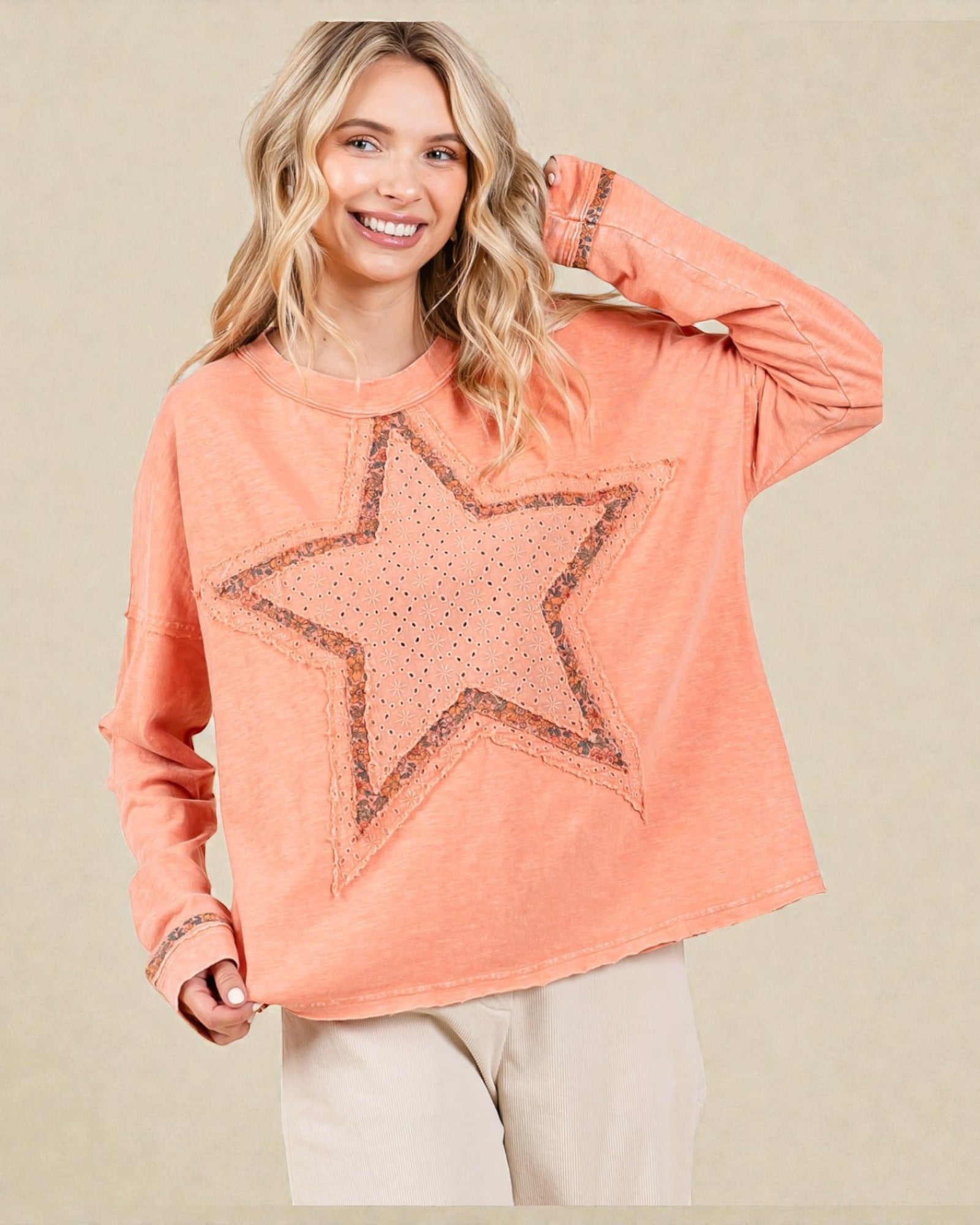 Woman wearing a peach-colored sweatshirt with a star design on a beige background