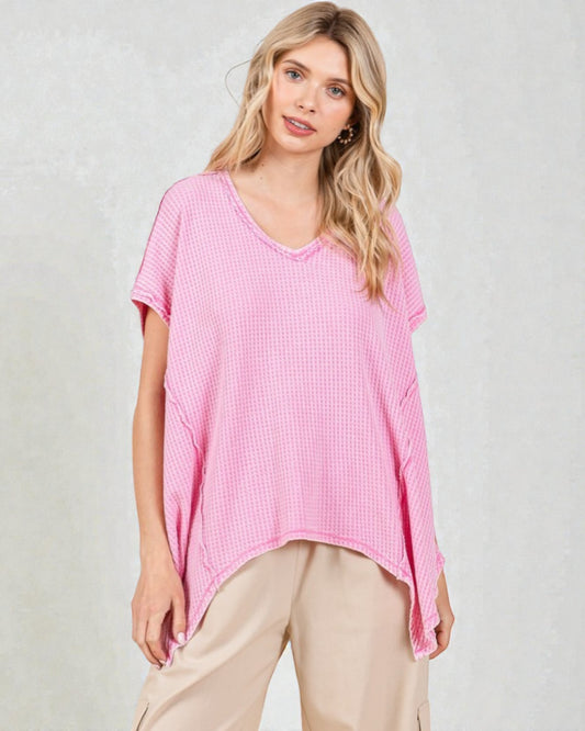Woman wearing a pink textured top and beige pants on a light background