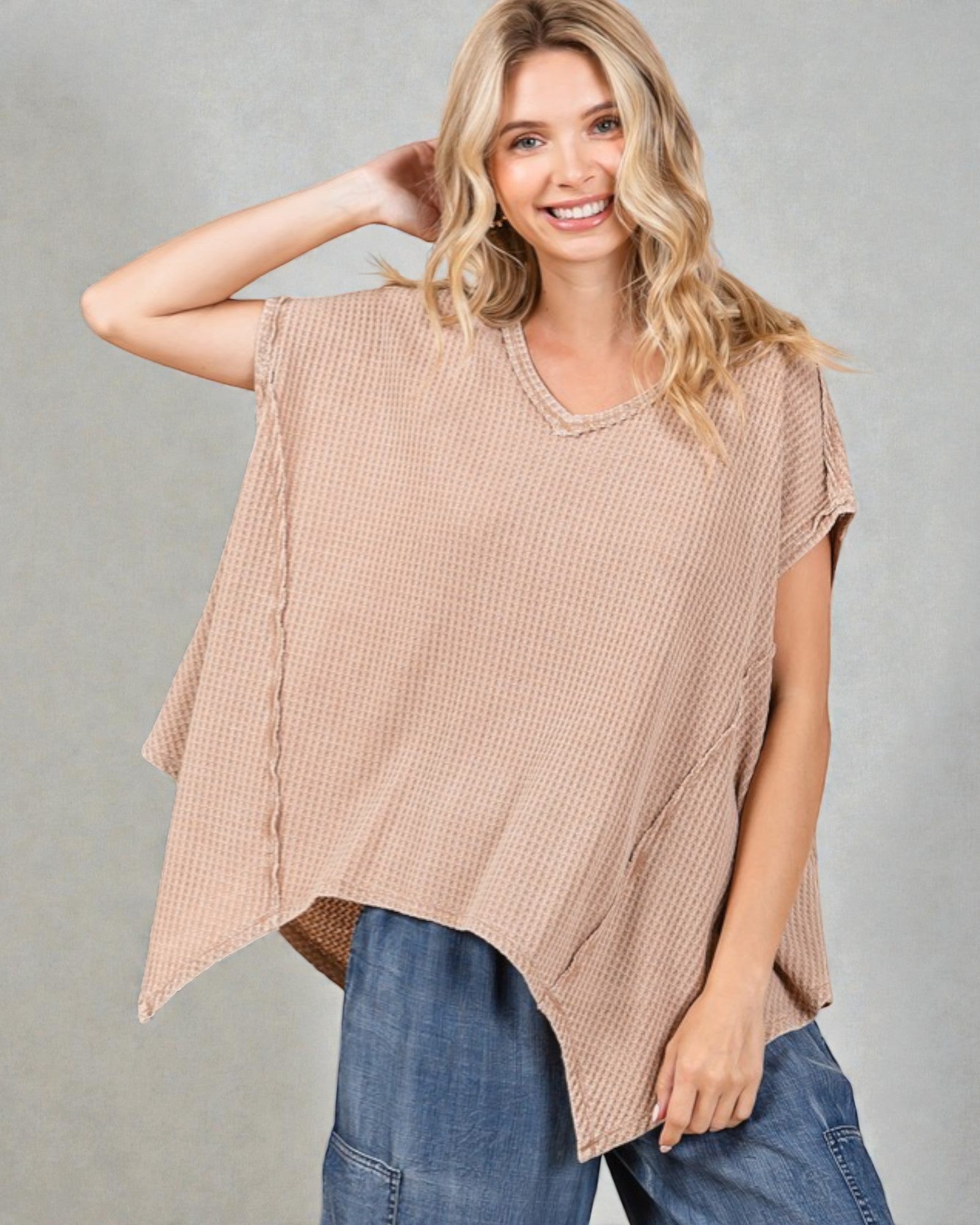 Woman wearing a beige oversized shirt and blue jeans against a gray background