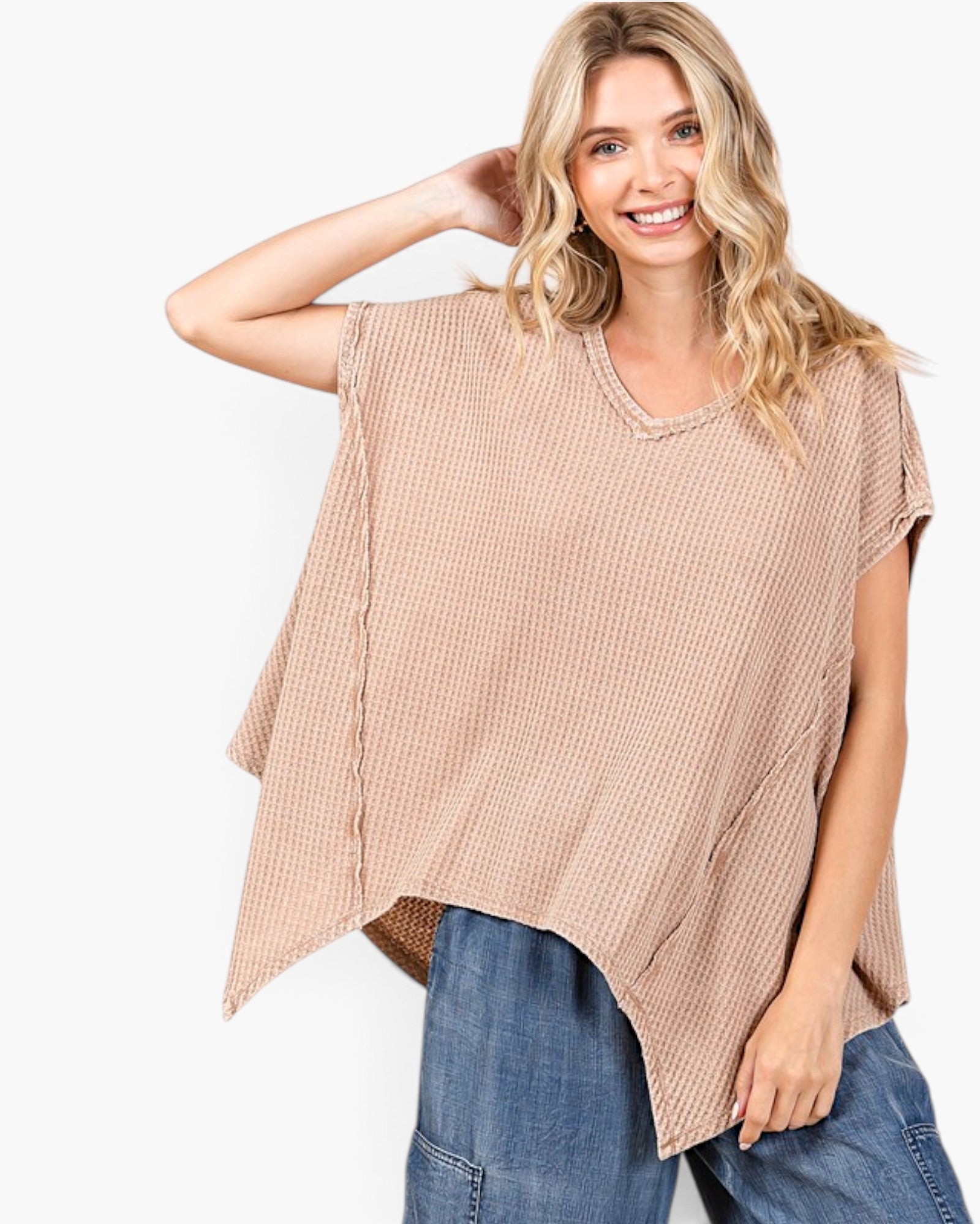 A woman wearing a loose, short-sleeve waffle-knit top in a light beige or tan color, paired with blue jeans, against a plain white studio background.