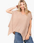 A woman wearing a loose, short-sleeve waffle-knit top in a light beige or tan color, paired with blue jeans, against a plain white studio background.