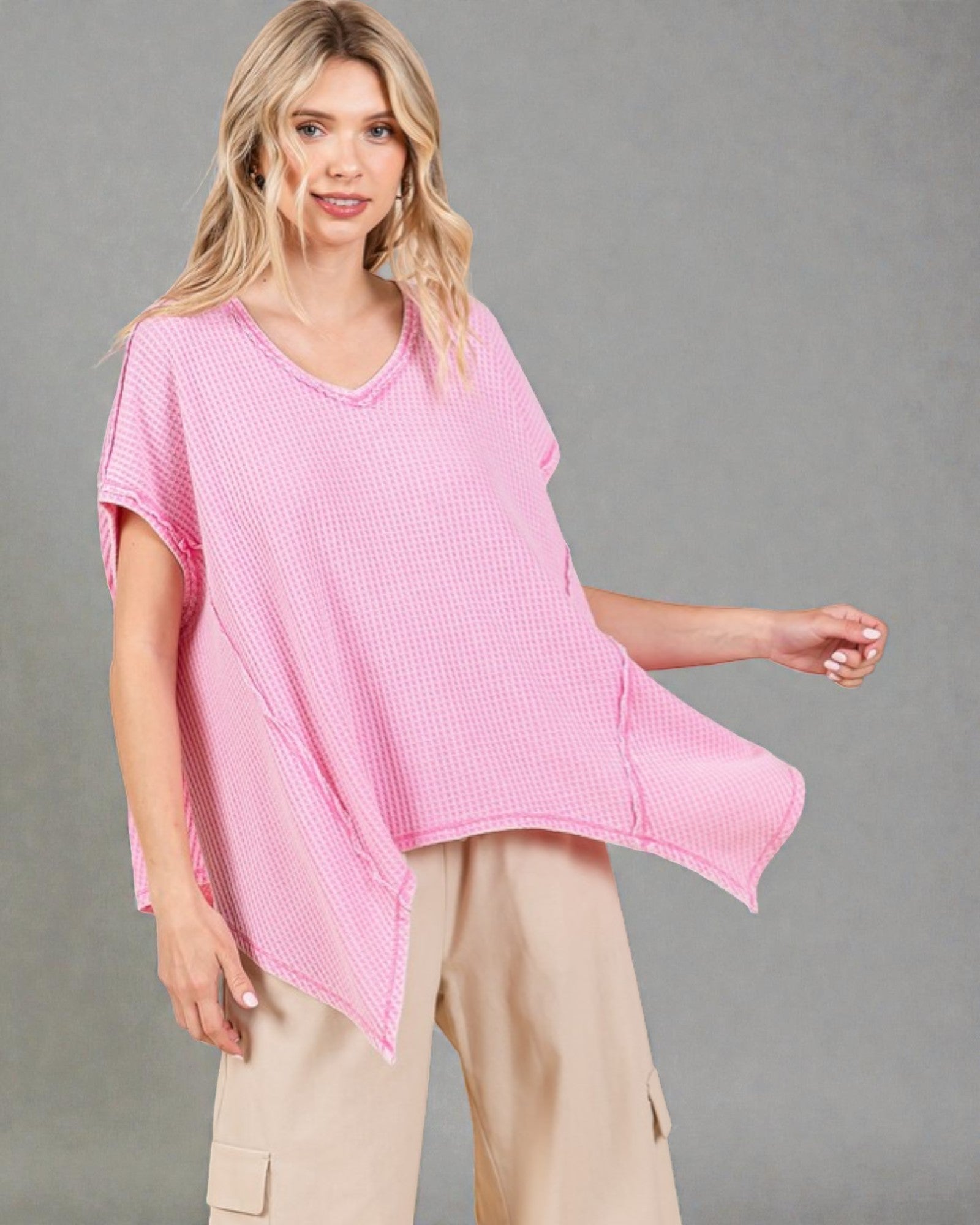 Woman wearing a pink oversized top and beige pants against a gray background