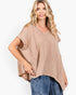 A woman wearing a beige waffle-knit short-sleeve top with a V-neck and side cutouts, paired with blue jeans, against a plain white background.