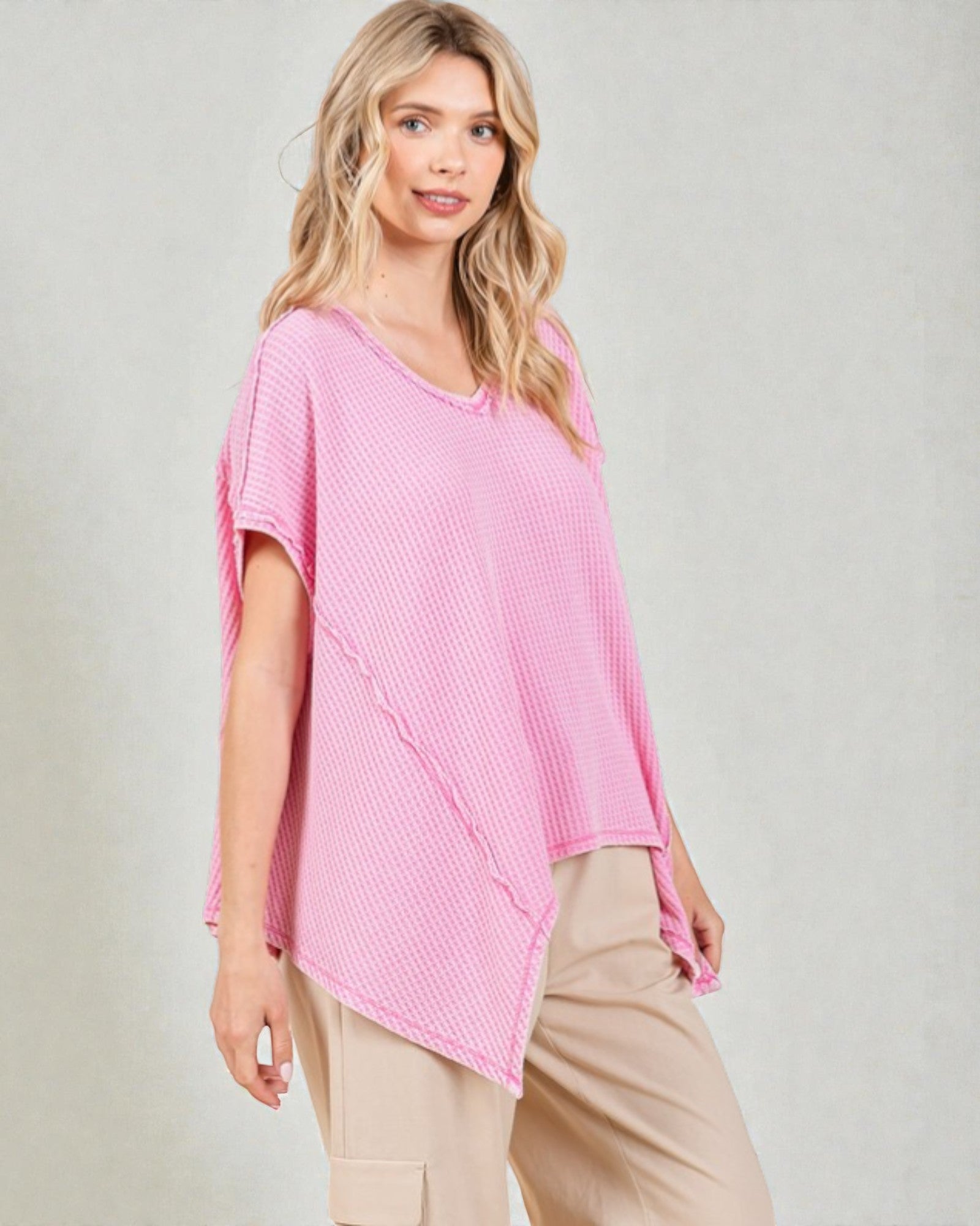 Woman wearing a pink textured top and beige pants on a plain background