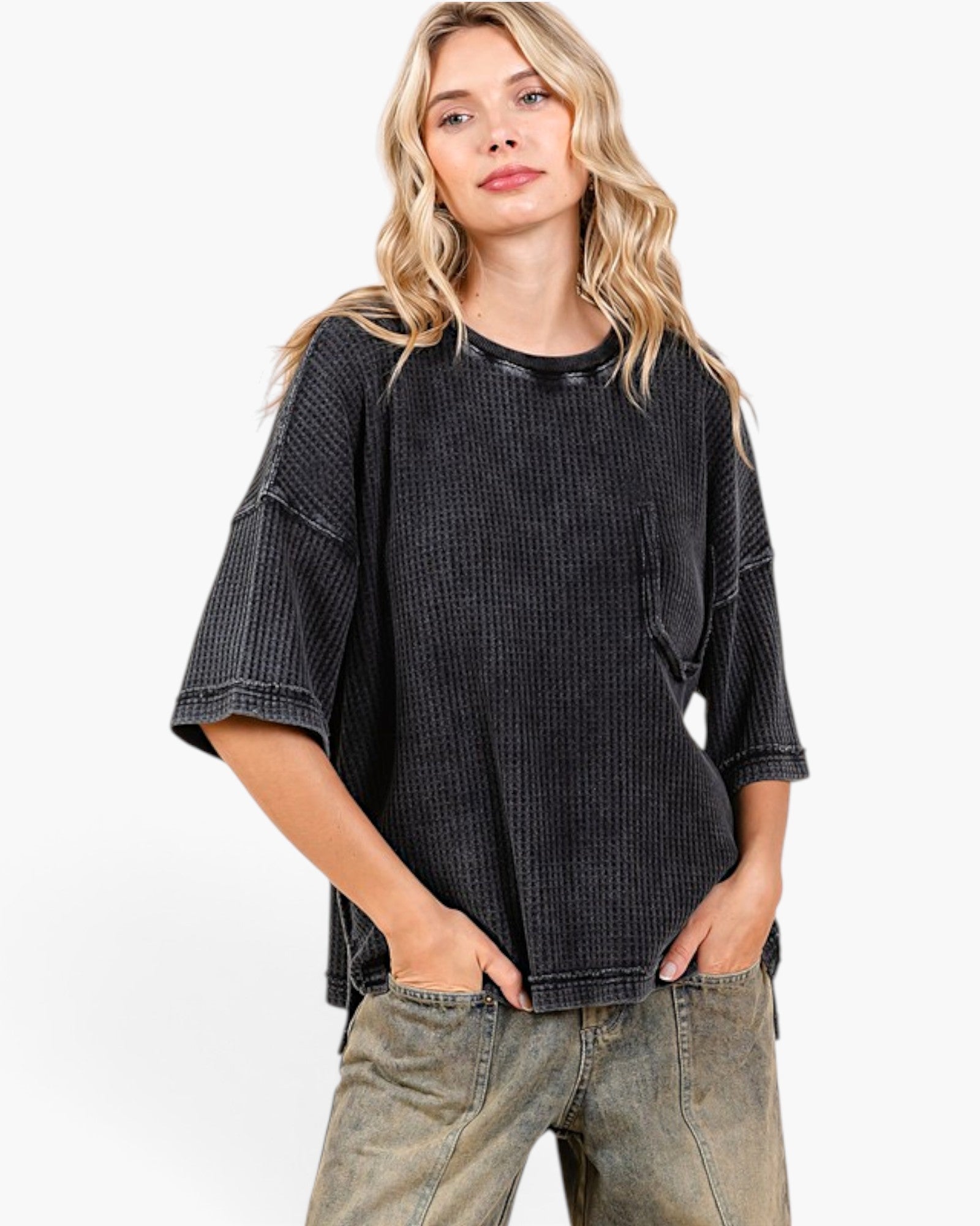 A woman modeling a washed black waffle-knit short-sleeve top with a crew neck and relaxed fit, paired with faded gray jeans, against a plain white studio background.