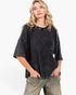A woman modeling a washed black waffle-knit short-sleeve top with a crew neck and relaxed fit, paired with faded gray jeans, against a plain white studio background.