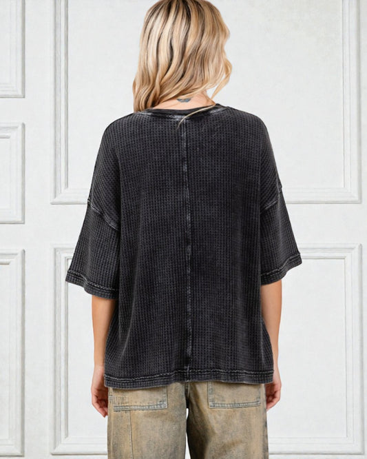 Person wearing a black textured shirt with a white paneled wall background