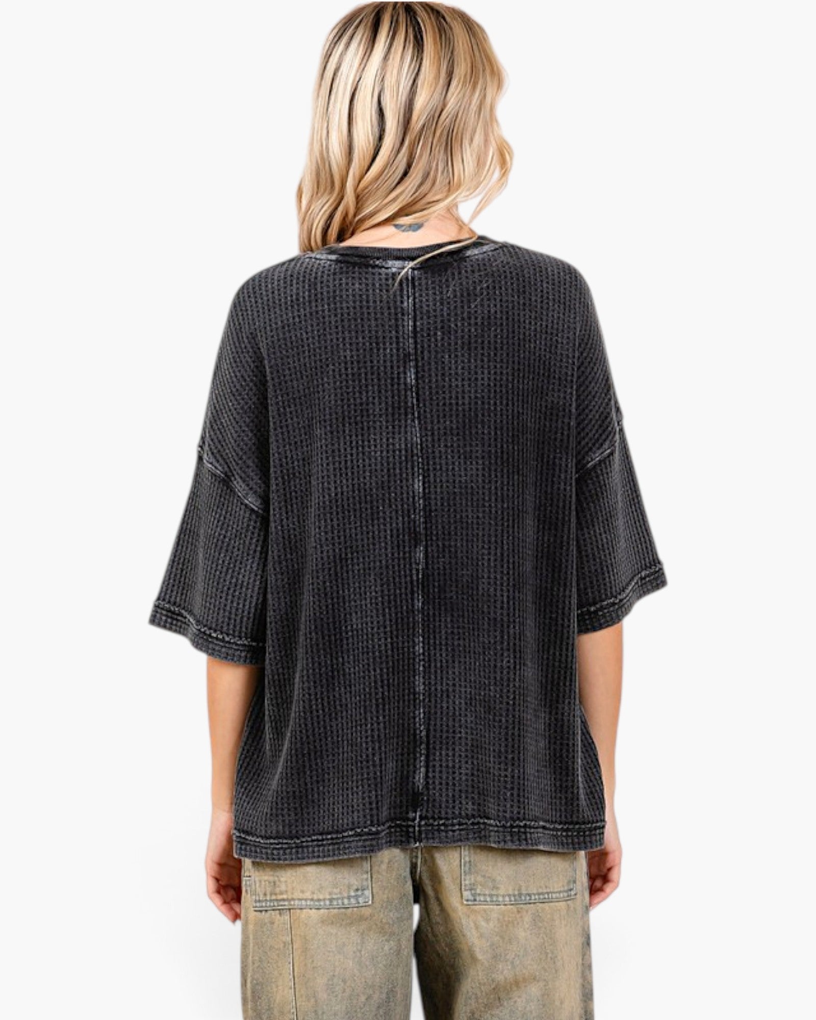 A woman shown from the back wearing a dark washed, textured short-sleeve top and light-wash jeans against a plain white background.