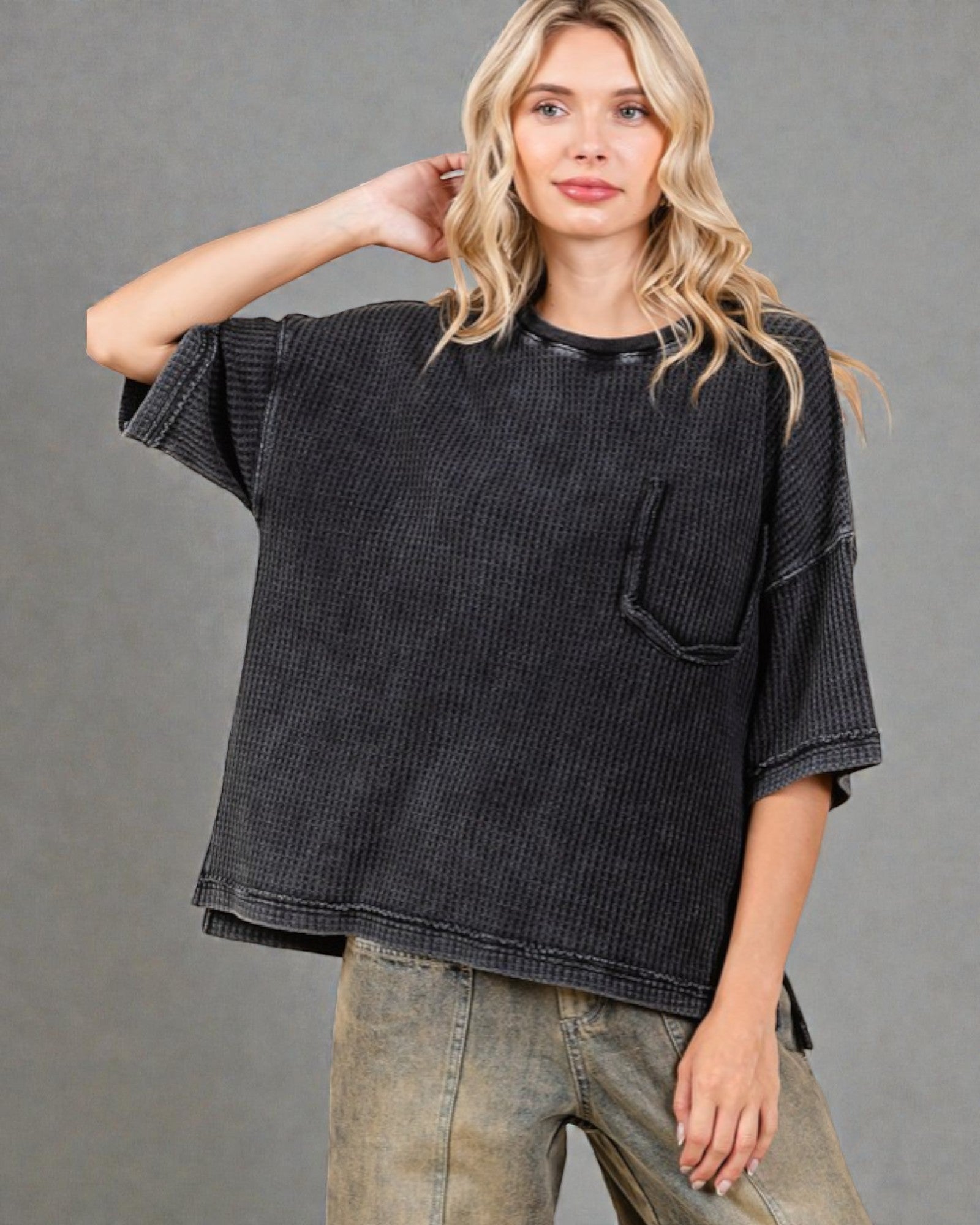 Woman wearing a black textured shirt with a pocket on a gray background