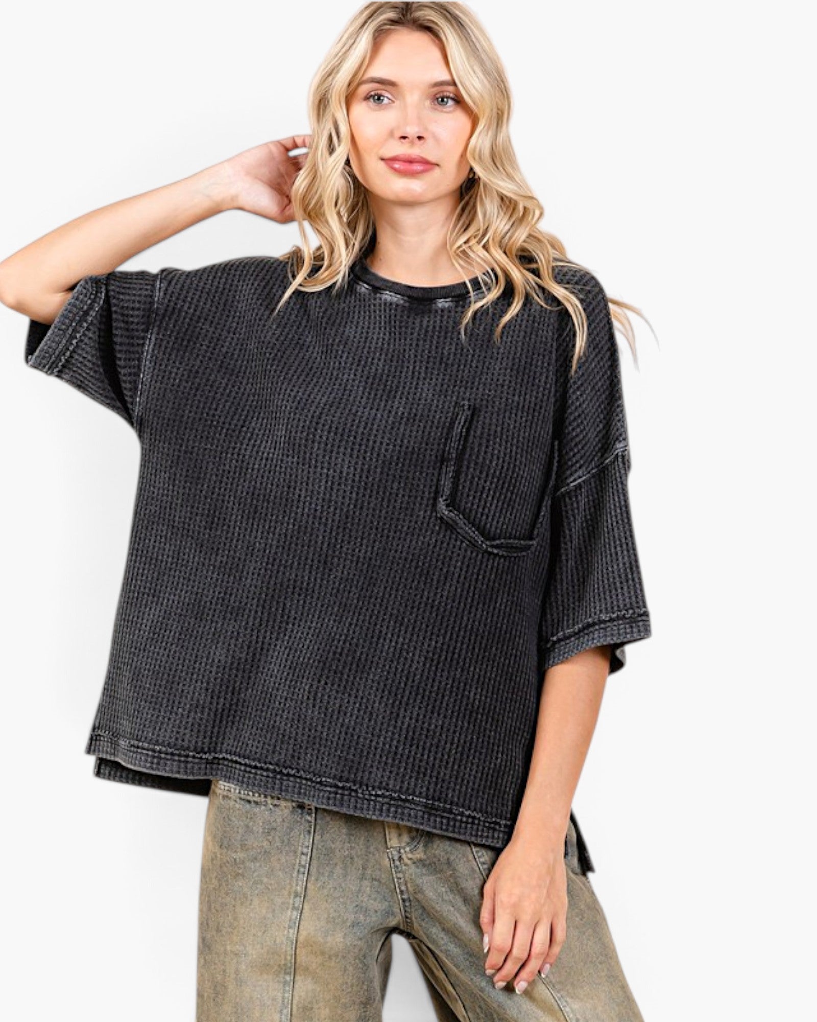 A woman modeling a washed black short-sleeve waffle-knit top with a chest pocket, paired with faded blue jeans, against a plain white background.
