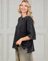 Woman wearing a black textured sweater and jeans against a light gray wall.