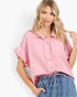 A woman wearing a light pink textured short-sleeve button-up shirt with ruffled cuffs and blue denim drawstring shorts, posed against a clean white background.