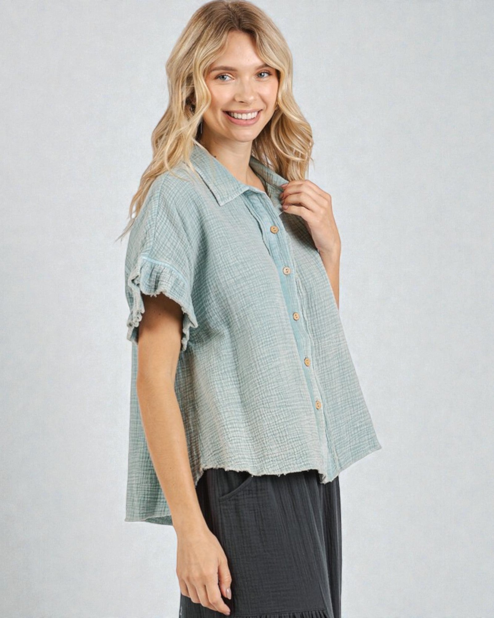 Woman wearing a light blue textured shirt with ruffled sleeves on a plain background