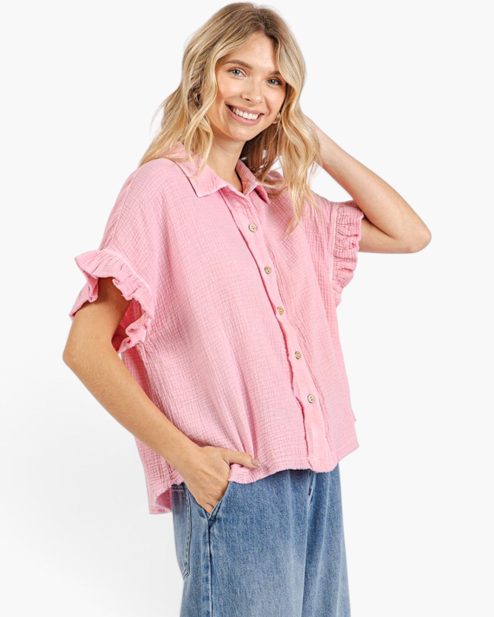 A woman modeling a light pink short-sleeve button-up shirt with ruffled cuffs and a textured waffle fabric, paired with blue jeans against a plain white background.