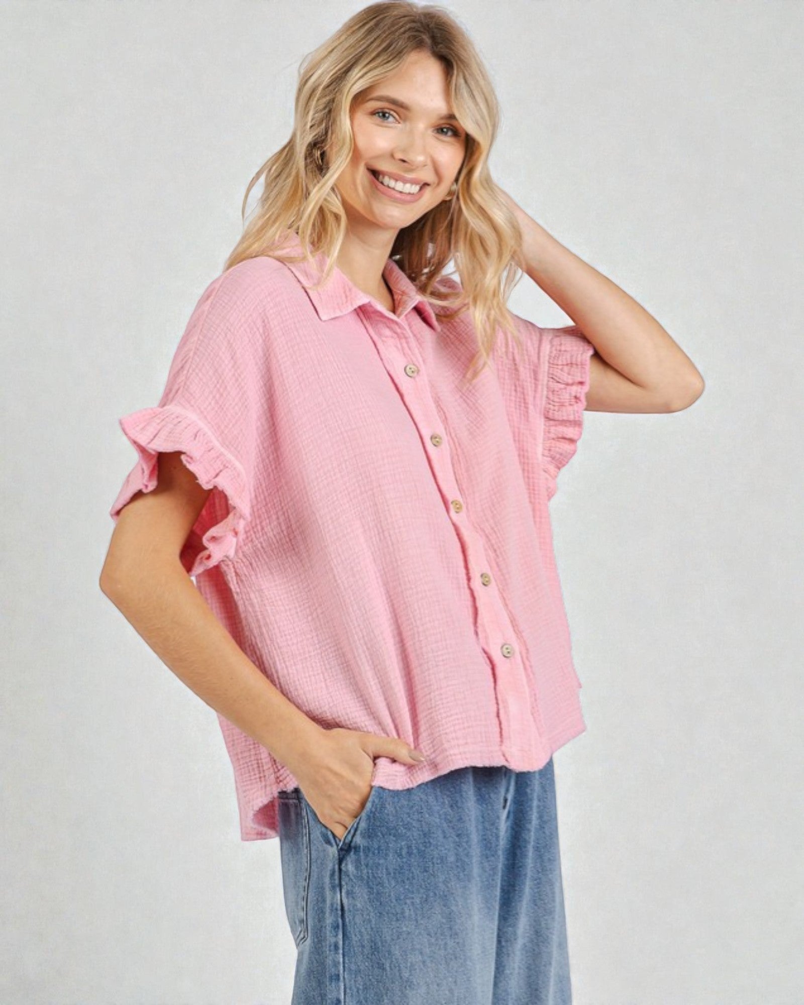 Woman wearing a pink blouse with ruffled sleeves on a plain background