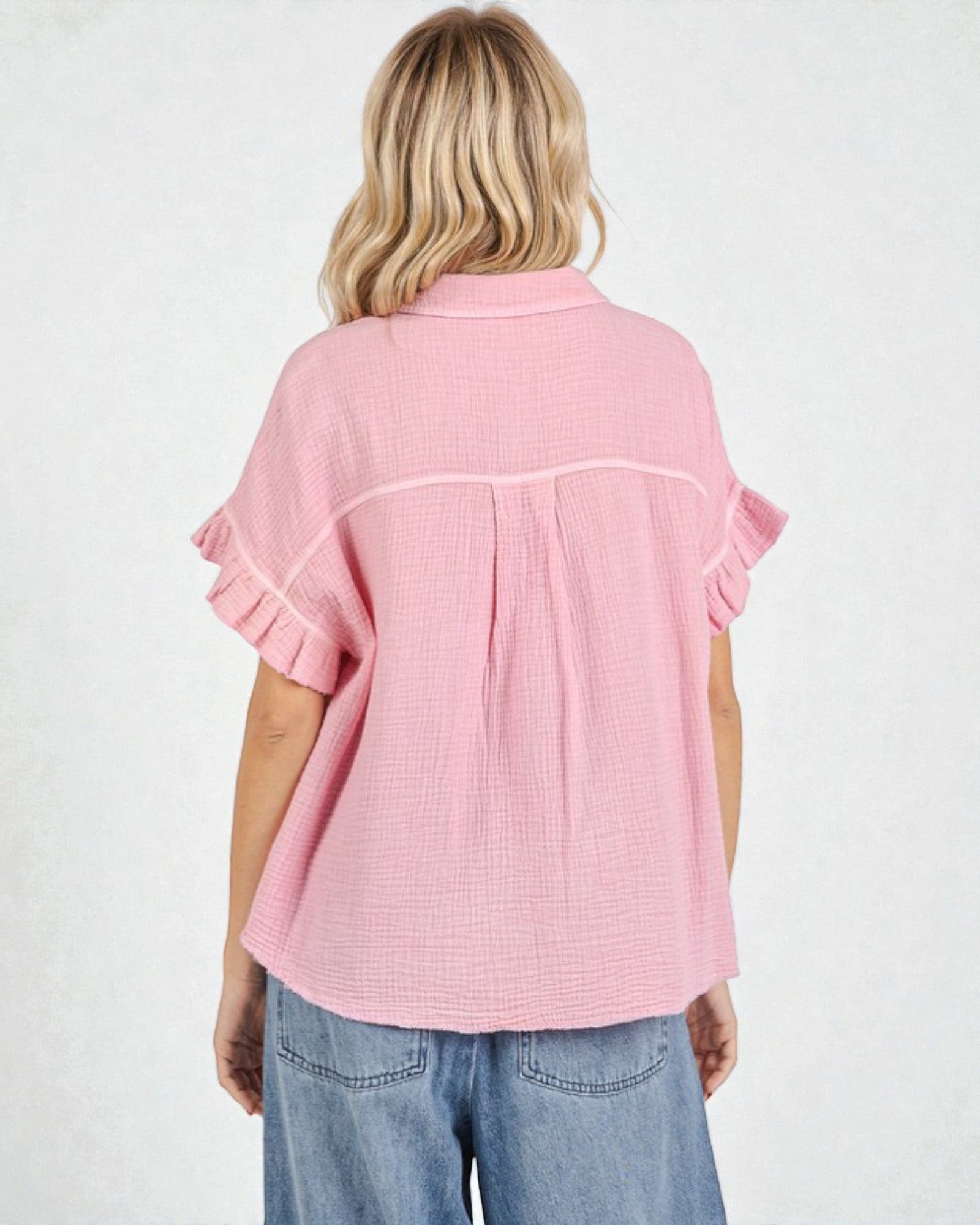 Person wearing a pink textured shirt with ruffled sleeves on a white background