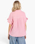 A woman viewed from the back wearing a light pink textured short-sleeve blouse with ruffled cuffs and a pleated back detail, paired with blue jeans against a plain white background.