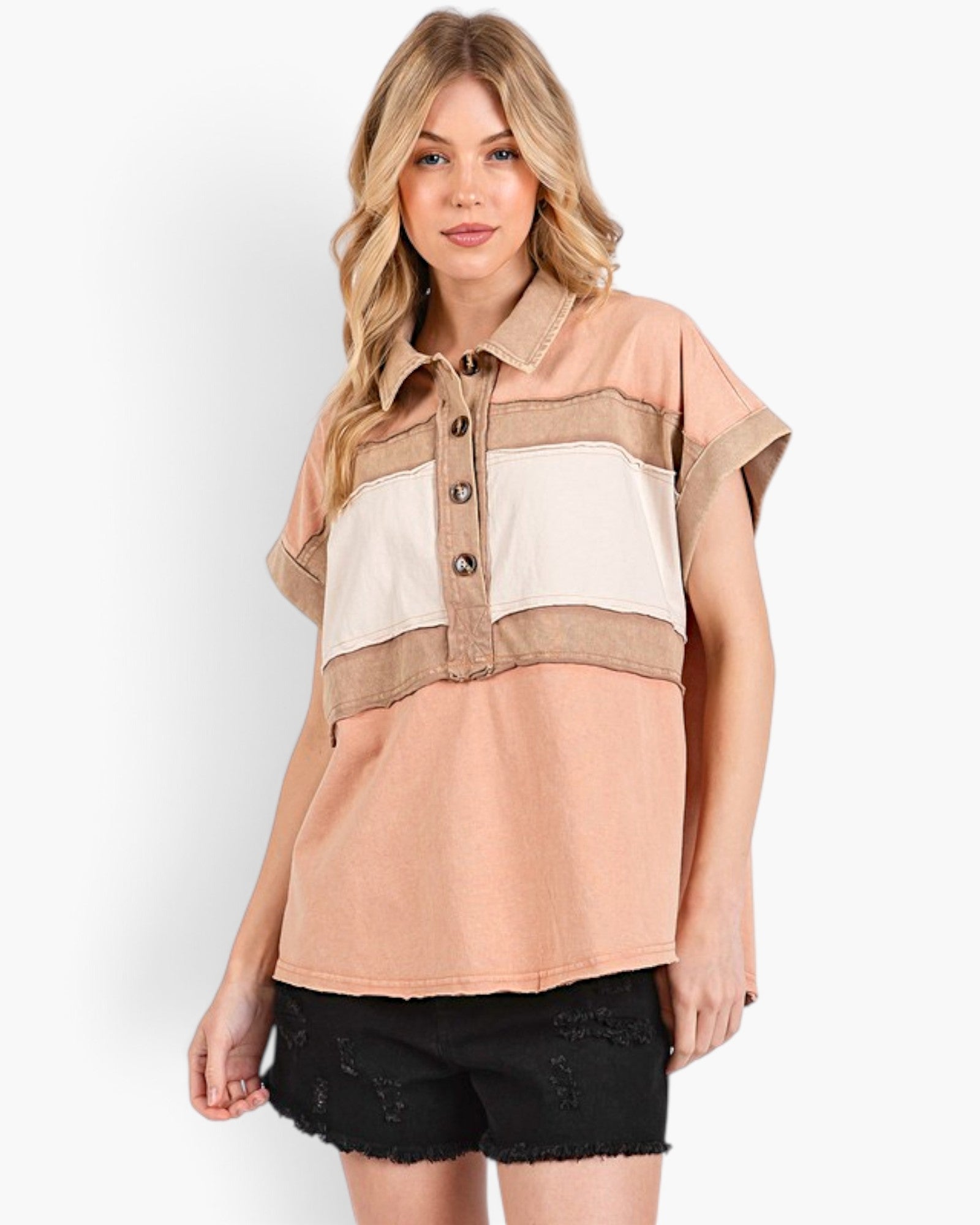 A woman modeling a short-sleeve color-block button-up shirt with peach, beige, and off-white panels, paired with black shorts, against a plain white studio background.