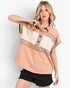 A woman modeling a short-sleeve color-block shirt with a peach, beige, and cream design, paired with black distressed denim shorts, against a light gray studio background.
