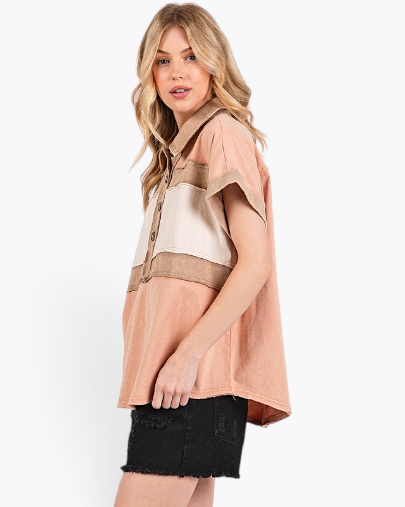 A woman modeling a short-sleeve color-block shirt in peach, beige, and cream, paired with a black denim skirt, against a plain white studio background.