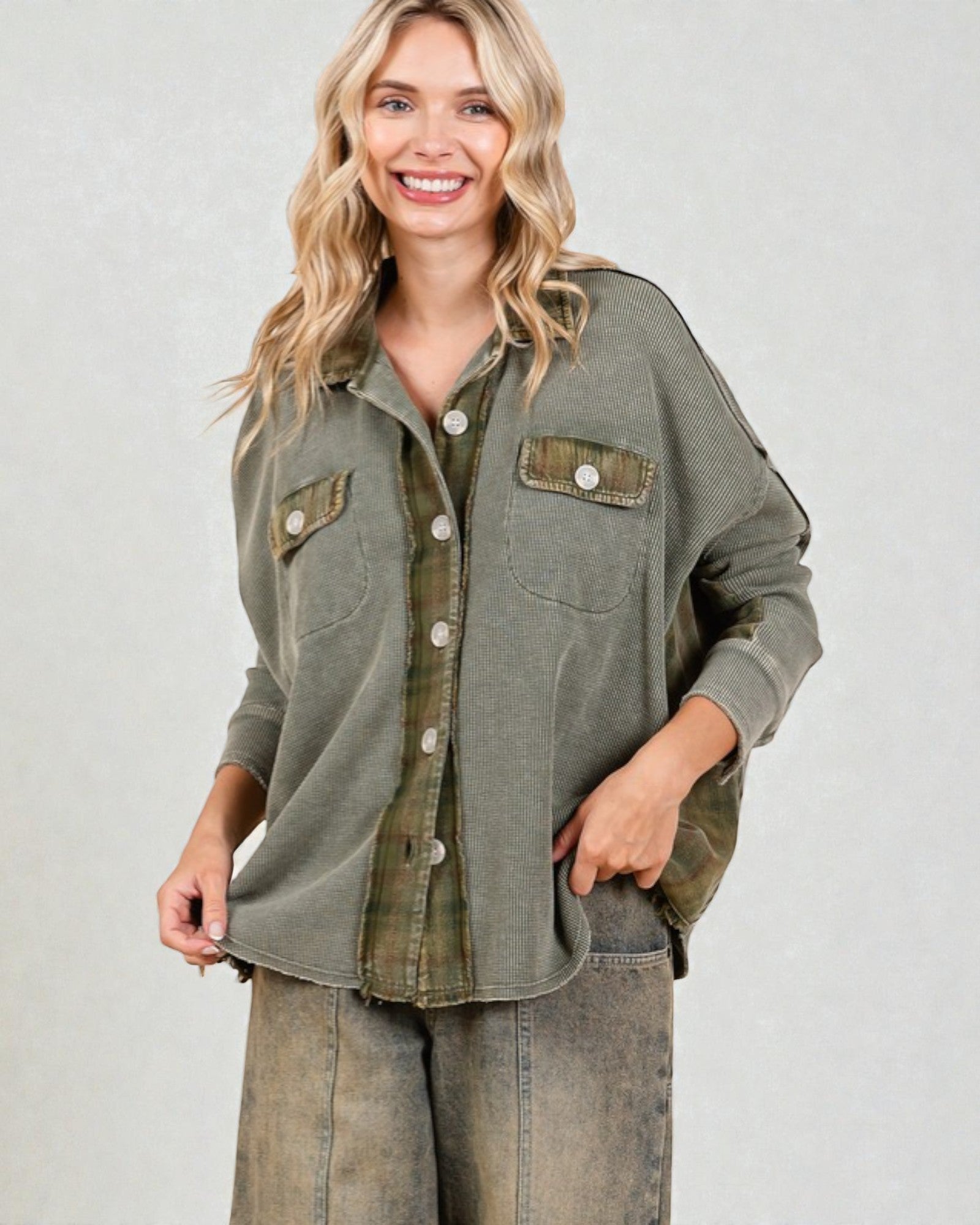 Woman wearing an olive green button-up shirt with rolled-up sleeves on a plain background