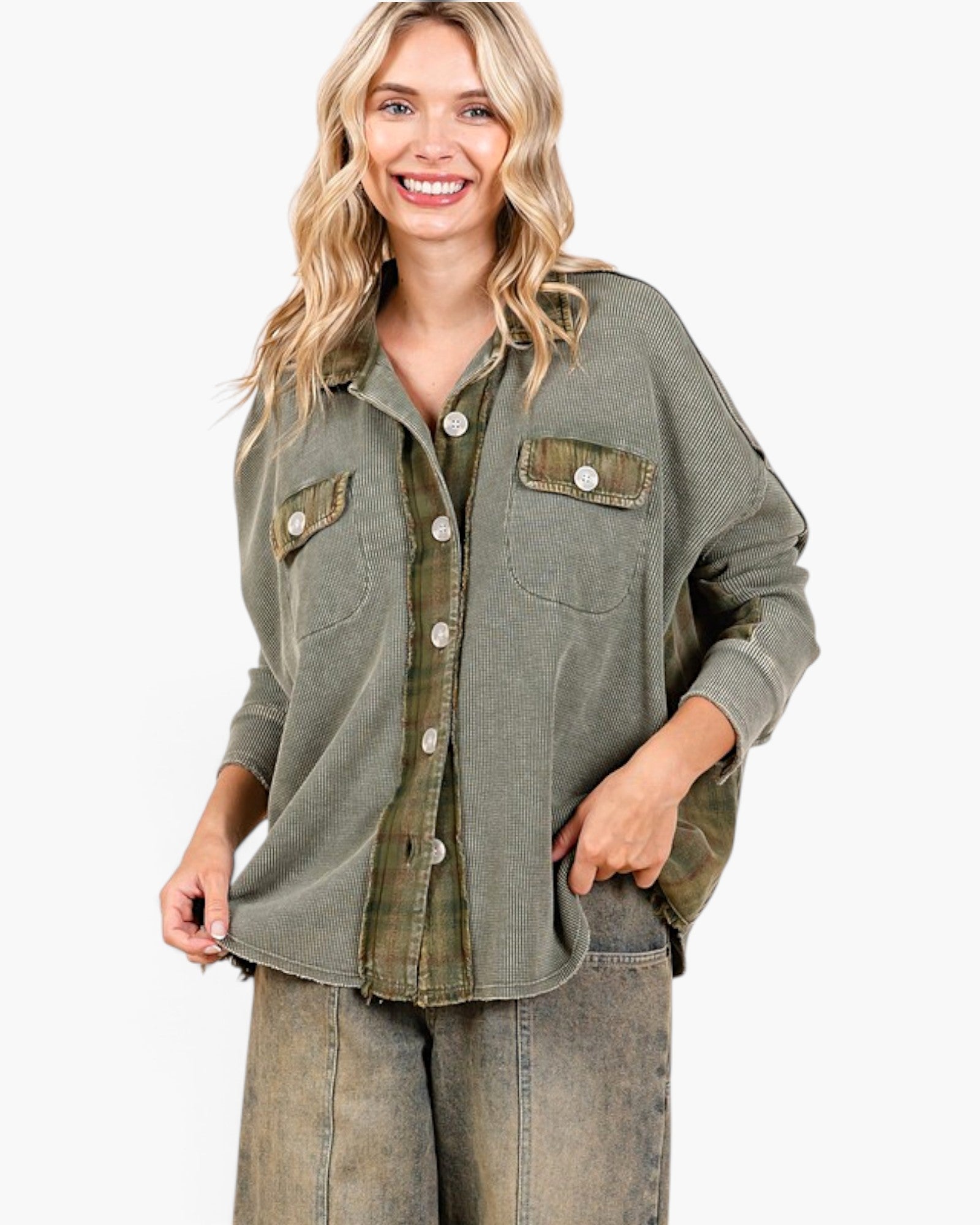 A woman wearing an oversized olive green button-up shirt with flap chest pockets and a plaid undershirt, paired with faded gray jeans, against a plain white background.