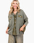 A woman wearing an oversized olive green button-up shirt with flap chest pockets and a plaid undershirt, paired with faded gray jeans, against a plain white background.