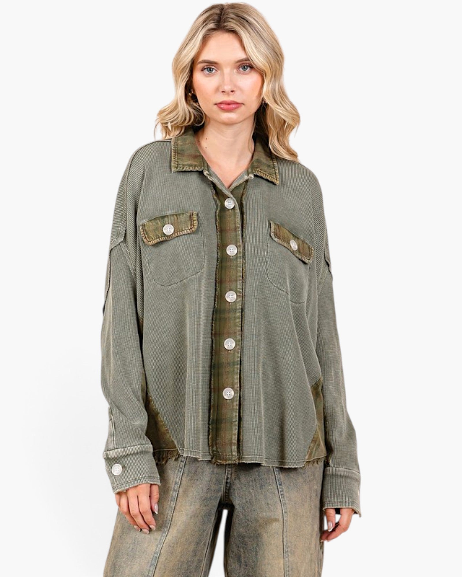 A woman modeling a washed olive green button-up shirt jacket with a plaid inner placket and matching chest pockets, paired with distressed gray jeans, against a plain white background.