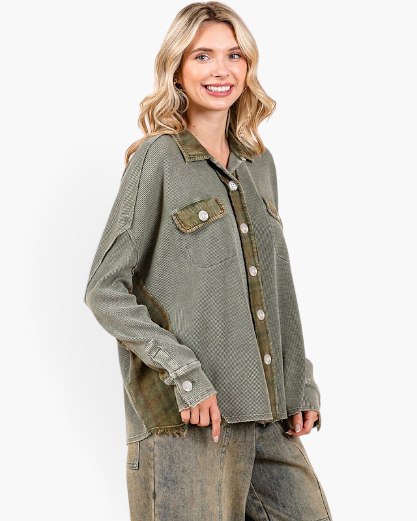 A woman wearing an oversized, washed olive green denim shirt jacket with button-front closure and flap chest pockets, paired with distressed denim pants, against a plain white studio background.