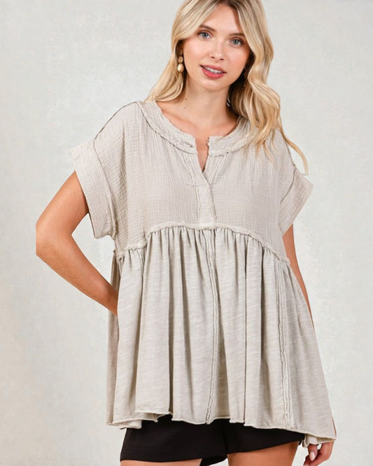 Woman wearing a beige short-sleeve top against a plain background