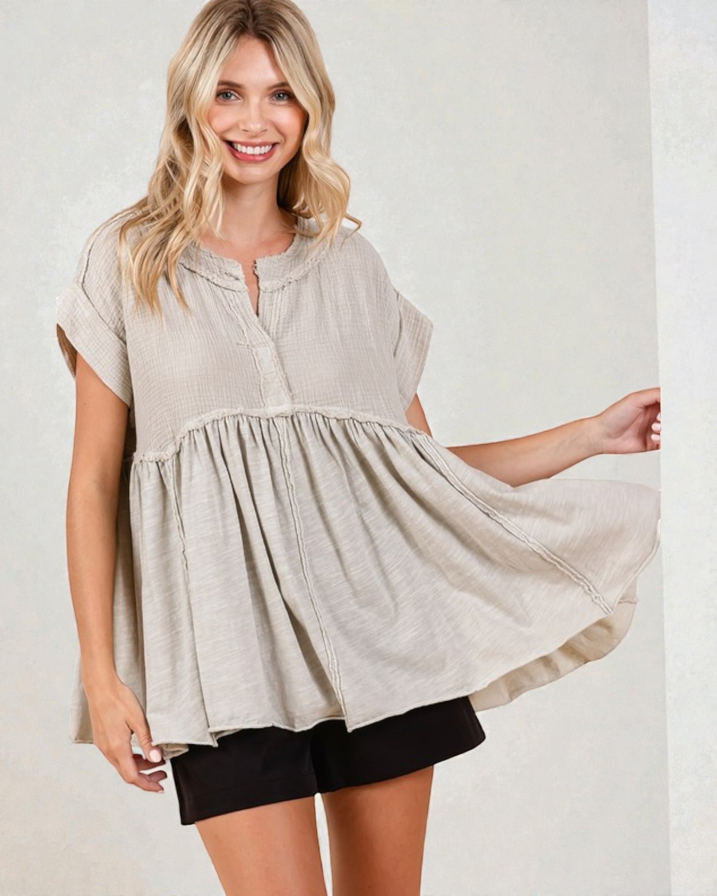 Woman wearing a beige short-sleeve top and black shorts on a plain background